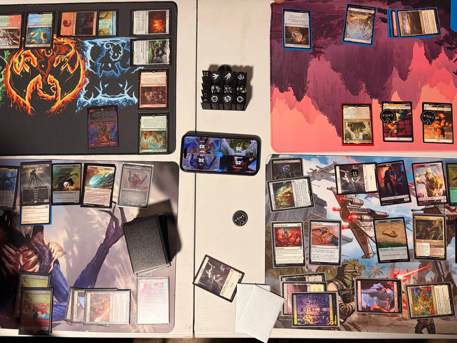 A four-player Commander table mid-game, with the TurnZero HQ life tracker running on a phone in the center