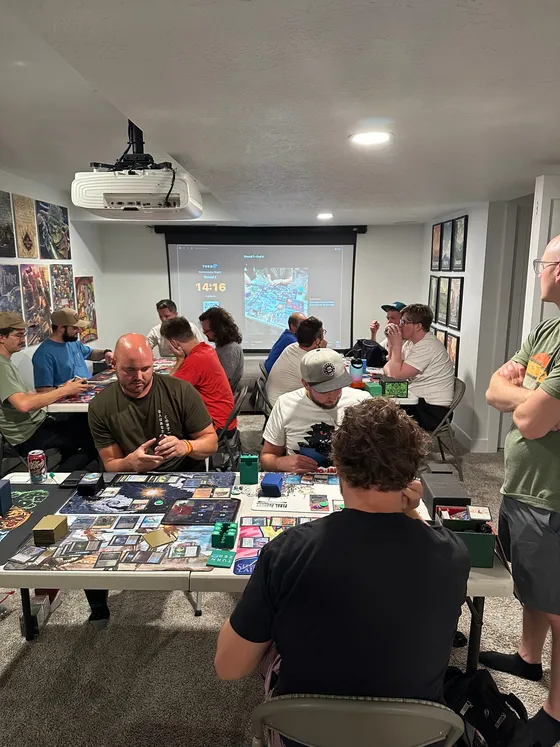 A room full of Commander players mid-game, with TurnZero HQ's TV mode up on the projector screen