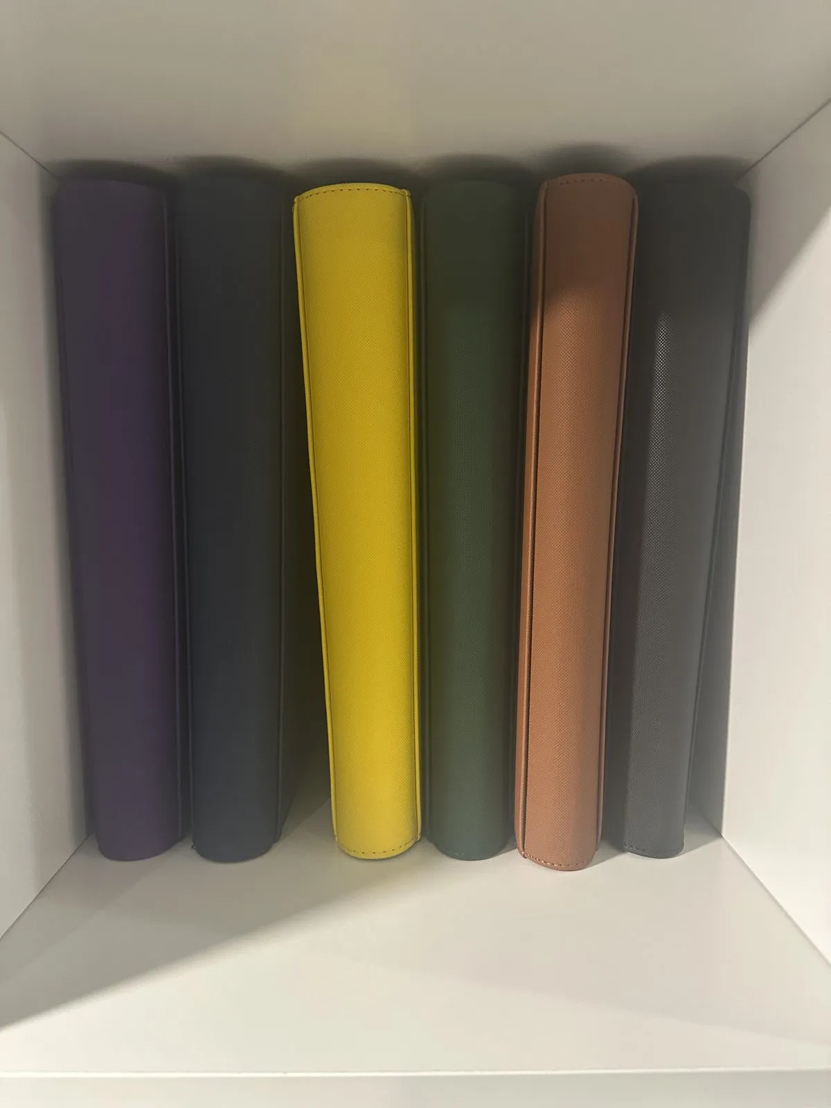 Six card binders in purple, slate, yellow, green, tan and gray standing on a shelf, one per color.